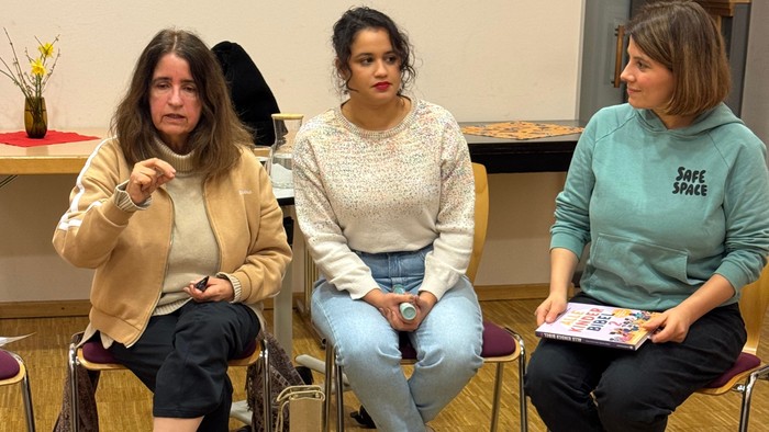 Drei Frauen, die in einem lockeren Innenraum auf Stühlen sitzen und in eine Diskussion oder Präsentation vertieft scheinen.