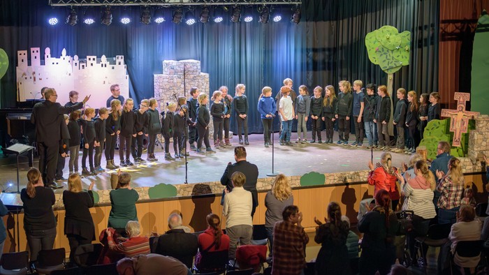Der Kinderchor tritt während eines festlichen Konzerts auf der Bühne auf, während die Zuschauer unten sitzen.