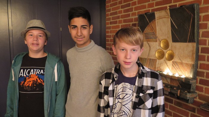 Tre drenge står sammen foran mur med billede og lysekilde.