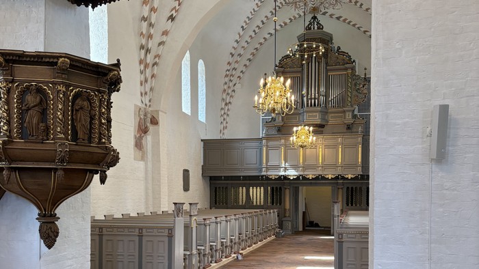 Indgang til en stor kirke med høje vægge og orgel.