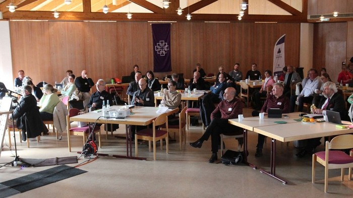 Eine Gruppe von Personen versammelte sich in einem Konferenzraum während eines formellen Treffens oder Seminars mit aufgestellten Tischen und Stühlen.