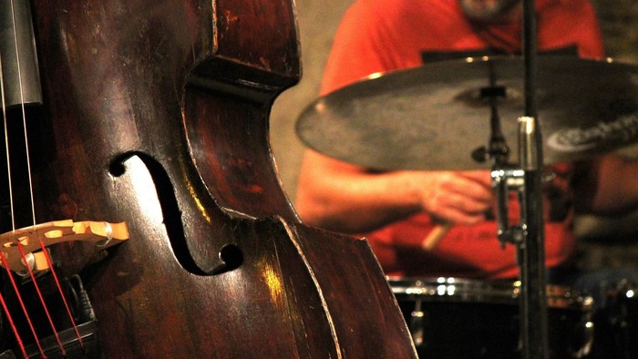 Ein Kontrabass im Vordergrund, im Hintergrund spielt ein Mann Schlagzeug