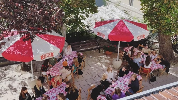 En ude spisested med røde paraplyer og folk der spiser og snakker.