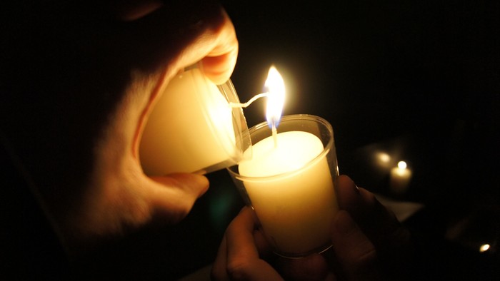 Eine Person, die eine Kerze in einer schwach beleuchteten, feierlichen Umgebung anzündet, während eine andere Kerze bereits brennt.