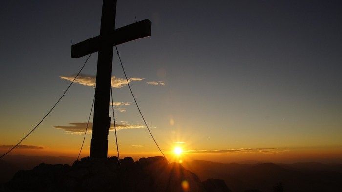 Sonnenaufgang mit einem Gipfelkreuz im Vordergrund