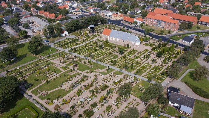 Luftfoto af en velholdt kirkegård omgivet af et charmerende, træbevokset boligkvarter.