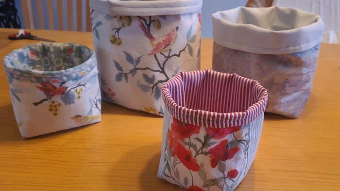 Handgefertigte stoffbezogene Behälter mit Blumenmustern und gestreiftem Besatz auf einer Holzoberfläche.