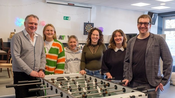 Eine Gruppe von Personen, die in einem Büro in der Nähe eines Tischkickers posieren.