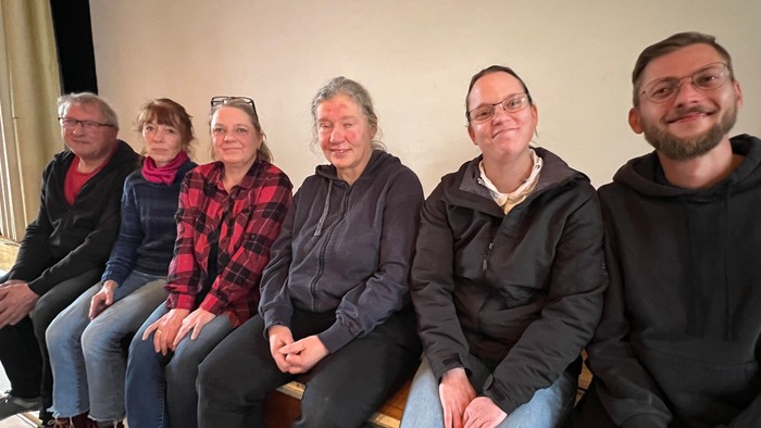 Sechs Menschen sitzen nebeneinander und schauen in die Kamera.