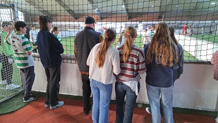 Eine Gruppe beobachtet ein Baseballspiel hinter einem Schutznetz in einem Stadion.
