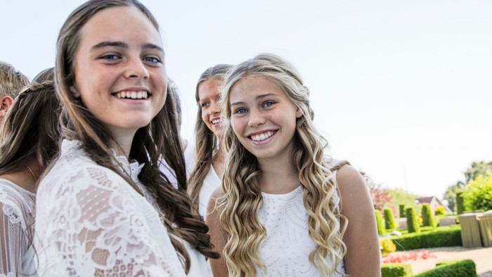 Glade unge kvinder i hvide kjoler, der smiler udendørs til en munter begivenhed.