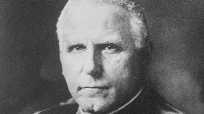 Ein älterer Mann mit weißen Haaren, der einen Anzug und eine Medaille trägt.