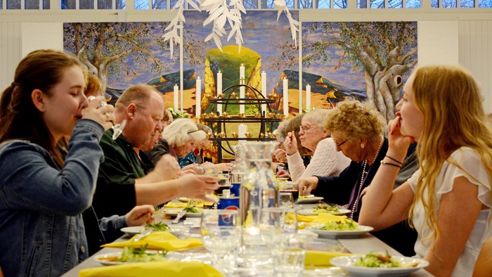 En festlig middagssammenkomst med mennesker, der nyder et måltid ved et langt bord pyntet med lys og dekorationer.