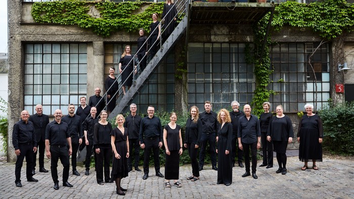 En gruppe af mennesker i sort klædning står sammen foran et grønt dækket bygning.