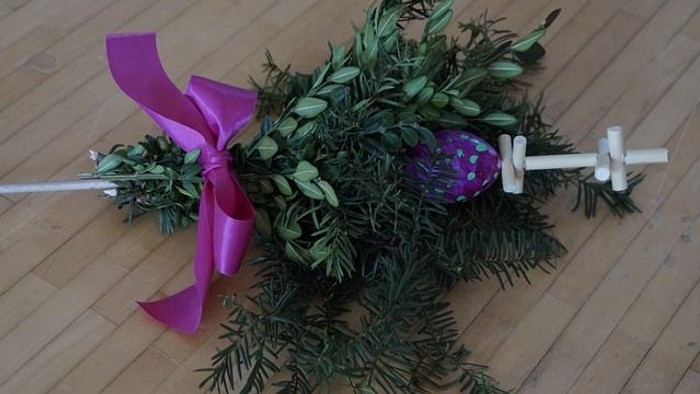 Ein mit Grünpflanzen und einer violetten Schleife dekorierter Stab mit Kreuz.