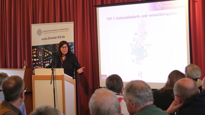 Ein Redner präsentiert vor einem aufmerksamen Publikum über Wohnungsnachfrage und Entwicklungspläne während einer Konferenz.