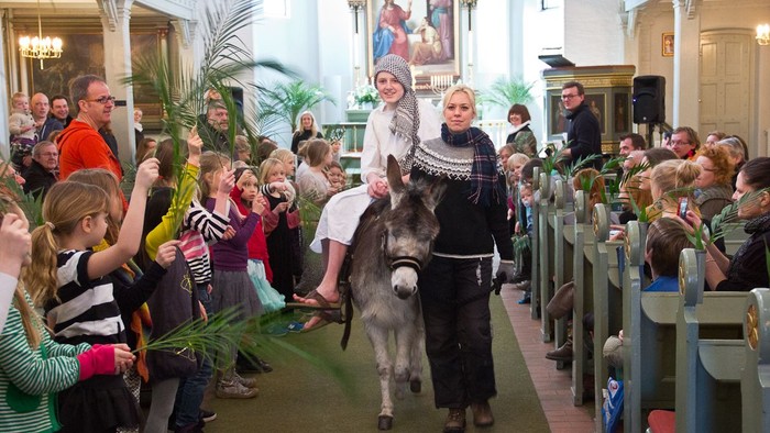 En gruppe børn og voksne deltager i en processjon med en esel og to personer i kostumer i en kirke.