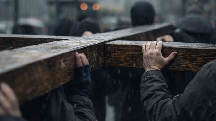 Ein Kreuz wird von mehreren Maennern, auf ihren Schultern, duch eine Strasse getragen.