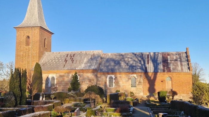 En kirke med tårn og en have med buske og stier