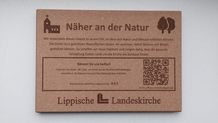 Brauner Holzschild mit Infos zu den Biodiversitätsmaßnahmen vor Ort und ein QR-Code für einen Biodiversitätszählbogen