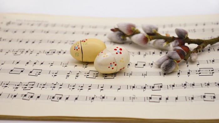 Zwei bemalte Ostereier und eine Blume liegen auf Notenblättern