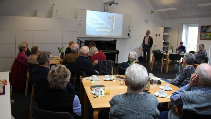 Mennesker i forgrunden ser på storskærm og foredragsholder