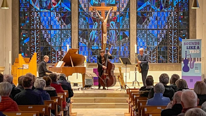 Drei Musiker am Flügel, am Kontrabass und am Saxophon in einem modern gestalteten Altarraum