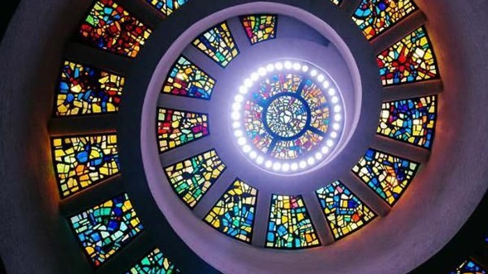 Plakat kündigt sonntägliche Gottesdienste mit spiralförmigem Buntglasdesign und Veranstaltungsterminen an.