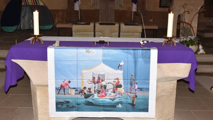 Verzierter Altartisch mit einem farbenfrohen Strandmotiv-Banner, Kerzen und religiösen Gegenständen.