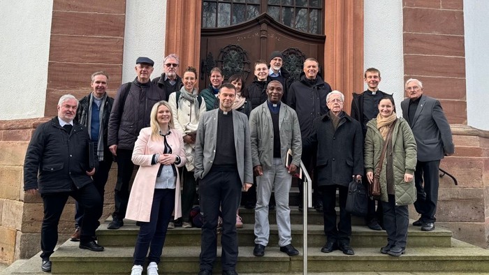 Gruppe von Menschen, die auf den Stufen einer Kirche vor dem Eingang eines historischen Steingebäudes posieren.