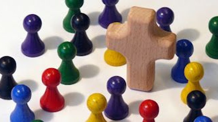 Bunte Plastikfiguren, die um einen hölzernen kreuzförmigen Block angeordnet sind.