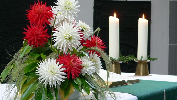 Blumenarrangement mit roten und weißen Blumen auf Tisch mit Kerzen und Buch