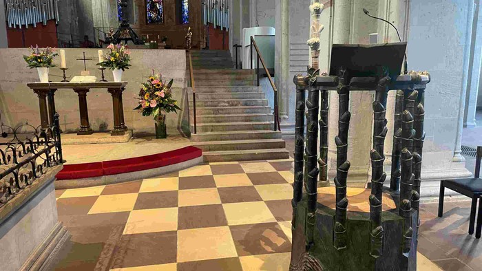 Elegante Kircheninnenausstattung mit Altar, kariertem Bodenbelag und einem dekorativen Taufbecken.