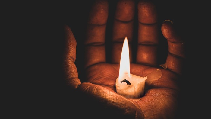 Eine Hand hält eine brennende Kerze im Dunkeln