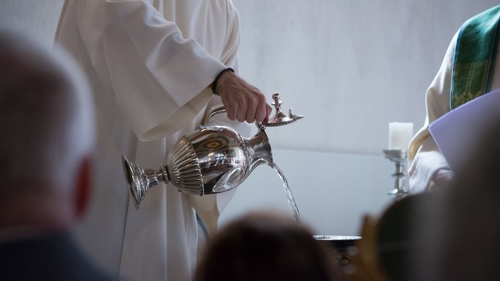 Ein Priester führt ein Ritual durch und gießt Wasser aus einem silbernen Aspergill während einer religiösen Zeremonie.