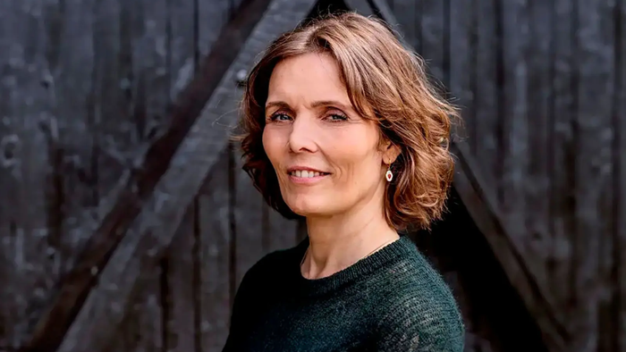 En smilende kvinde med kort brunt hår poser foran en mørk træbaggrund.