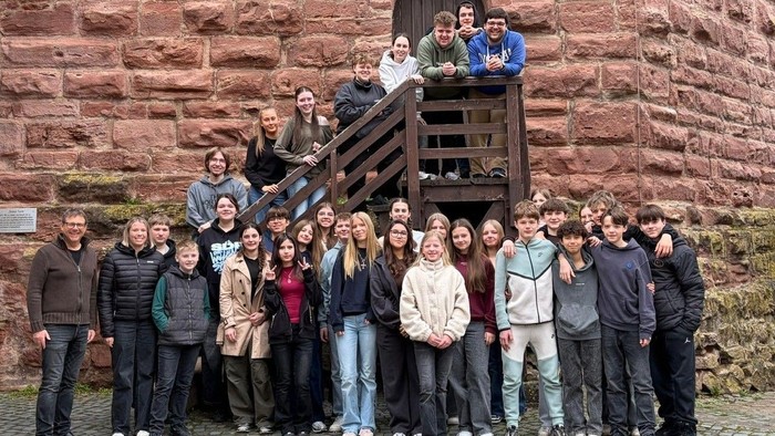 Gruppe von Studierenden, die gemeinsam vor einem alten Steingebäude mit einem Holzbalkon posieren.