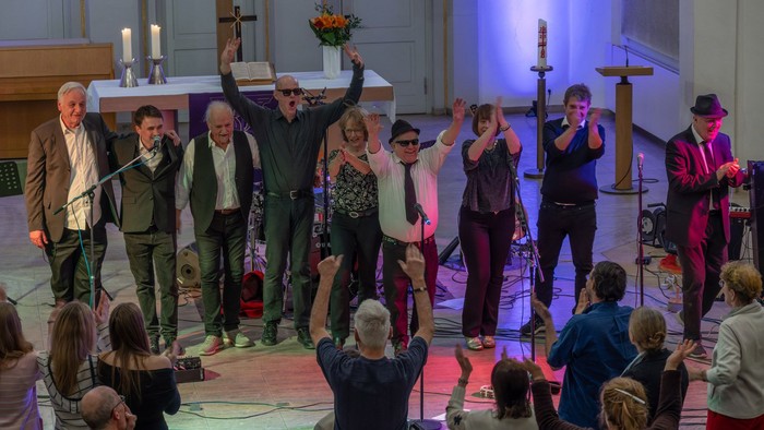 Eine fröhliche Gruppe feiert in einer Kirche mit erhobenen Händen, hält einen Blumenstrauß und singt gemeinsam.