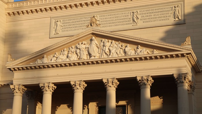 Das Bild zeigt ein klassisches Gebäude mit Säulen und aufwendigen Verzierungen.