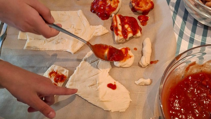 Barnehænder, der dekorerer pizzadej med tomatpuré.