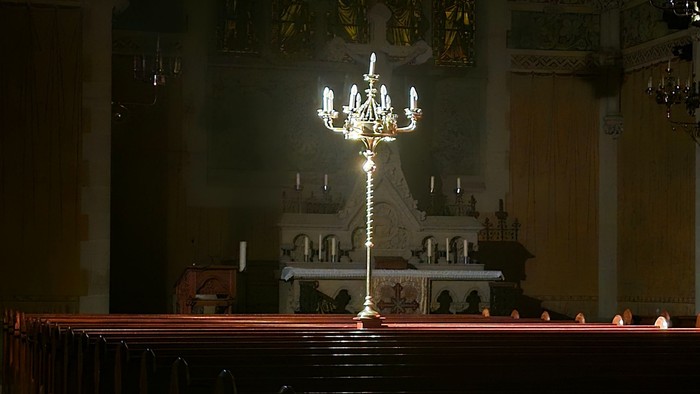 Elegante Kircheninnenausstattung mit beleuchtetem Kronleuchter und Reihen hölzerner Kirchenbänke unter einem gewölbten, verzierten Deckengewölbe.