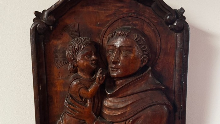 Aufwendig geschnitztes Holzrelief mit einer bekleideten Figur, die ein Kind hält, gerahmt mit verzierter Detailarbeit.