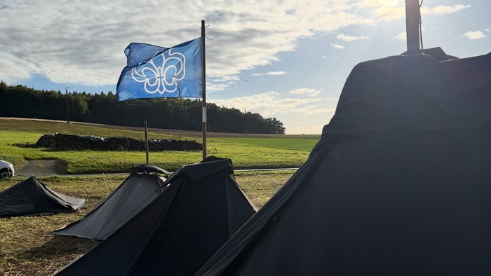 Campingplatz mit Zelten und einer Flagge mit einem weißen Kleeblattsymbol unter einem strahlend blauen Himmel.