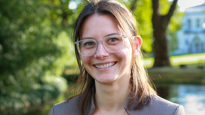 Eine junge Frau mit Brille und dunklen Haaren vor einem Teich im Park