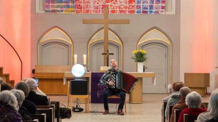 Musiker, der während eines Gottesdienstes Akkordeon spielt, mit einer aufmerksamen Gemeinde.
