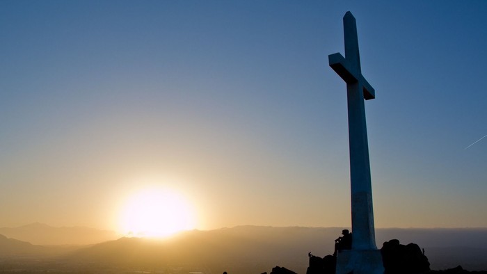 Ein Kreuz steht auf einem Felsen bei Sonnenuntergang.