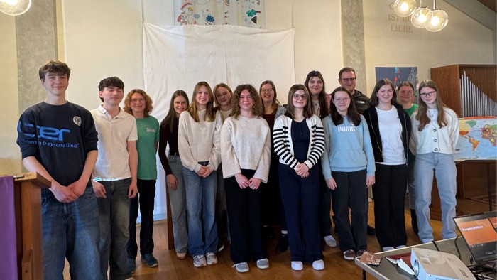 Gruppe von Studierenden, die drinnen gemeinsam vor einem dekorierten Banner und einer Orgel in einer kirchenähnlichen Umgebung posieren.