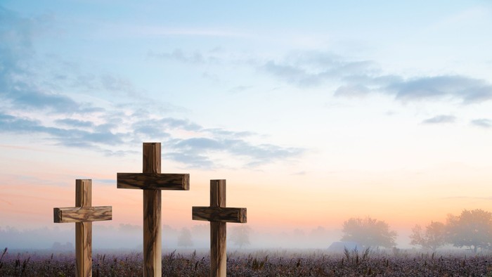 Das Bild zeigt drei Kreuze vor einem Himmel mit Sonnenuntergang