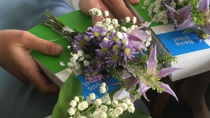 Eine Person arrangiert einen Blumenstrauß mit weißen und violetten Blumen auf einem grünen Blatt.