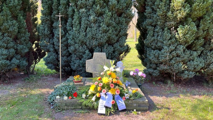 Ein Grabmal mit Blumen und Kerzen, umgeben von Bäumen und Gras.